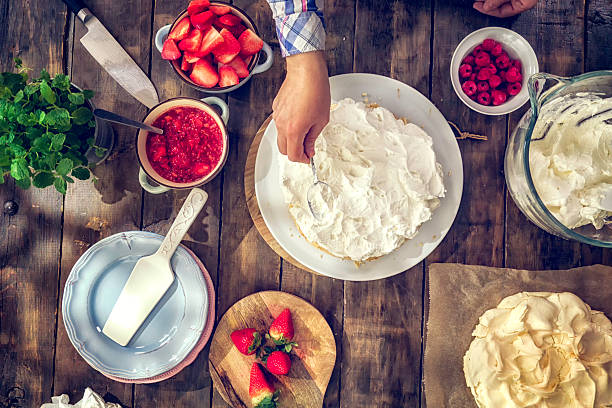 Preparing Berry Pavlova Cake with Strawberries and Raspberries Preparing Berry Pavlova Cake with fresh strawberries, raspberries, mint leaves and whipped cream. pavlova stock pictures, royalty-free photos & images