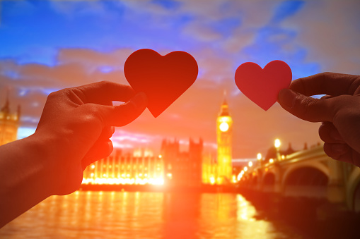 silhouette of romantic lovers hand hold love heart paper in Big Ben with sunset