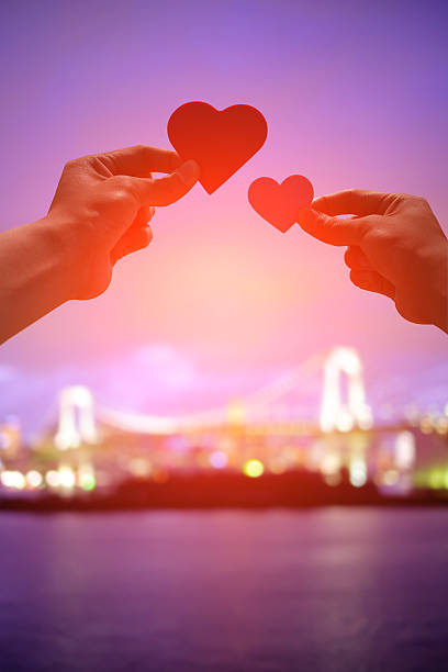 silhouette of romantic lovers hand hold love heart paper in Odaiba with sunset