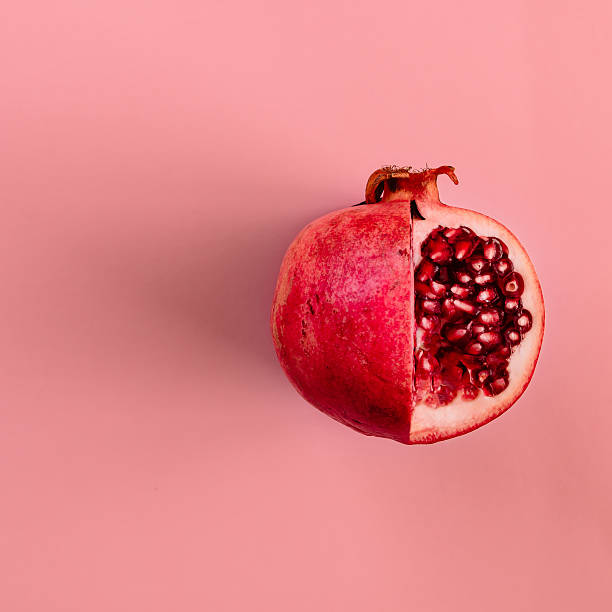 frutto di melograno rosso su sfondo rosa pastello. la piatta minima - melagrana foto e immagini stock