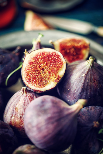 Whole and sliced figs on big fig leaves. Fresh ripe sweet fruits on dark background. Close-up. Selective focus. Blurred background.