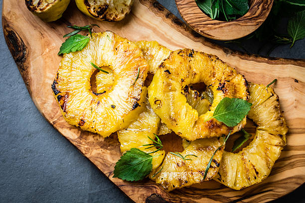 Grilled pineapple slices with fresh mint on olive cutting board Grilled pineapple slices with fresh mint on olive wooden cutting board, gray slate background. top view grilled stock pictures, royalty-free photos & images