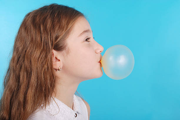 Girl blowing a big bubble gum bubble isolated on blue