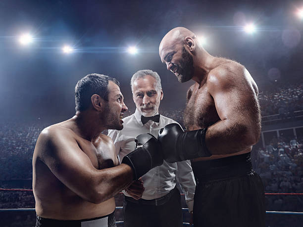 Boxing: Face to face A picture of two boxers face to face. Referee is between them. The sportsmen are on boxing ring with bleachers full of people. Sportsmen wear unbranded cloth. boxing referee stock pictures, royalty-free photos & images