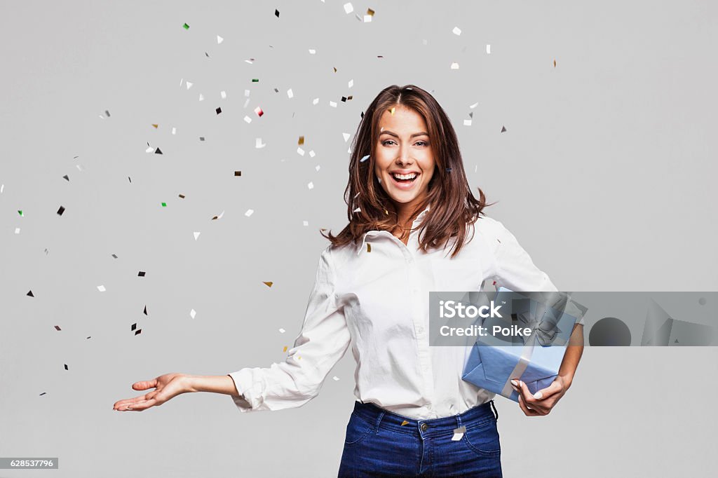 Laughing girl with falling confetti at party Beautiful woman with confetti and gift box at party on gray background Gift Stock Photo