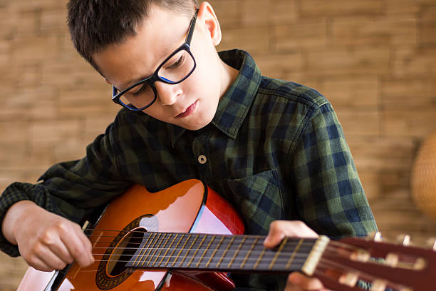 ragazzo con gli occhiali che suonano la chitarra acustica in soggiorno - guitar child music learning foto e immagini stock