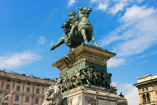 Close-up of The Monument to King Victor Emmanuel II, sculpted in 1896 by Ercole Rosa, Piazza del Duomo, Milan Italy. Fragment of the Palazzo Carminati and vivid blue sky with clouds are in background.