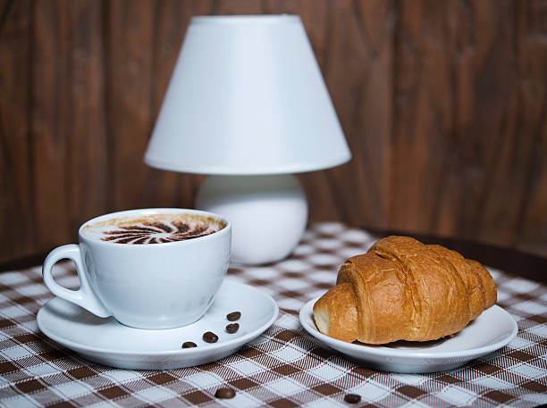 cup of cappuccino with croissant on a table
