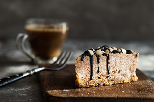 Healthy raw chocolate mousse cake  with cashew nuts, hazelnuts and dark chocolate glaze topping and coffee on a wooden and grey stone background. Vegan sugar, gluten, dairy free dessert. Dark food photography. Horizontal