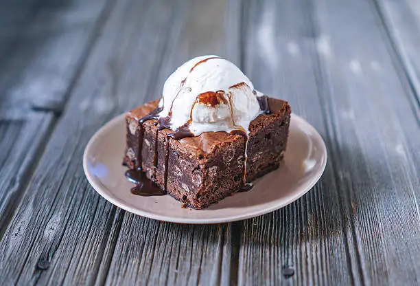 Chocolate Fudgy Brownie with Vanilla Ice Cream and Chocolate Syrup on Wood Background. Selective focus, toning.