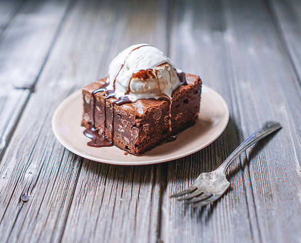 Chocolate Fudgy Brownie with Vanilla Ice Cream on top. Chocolate Fudgy Brownie with Vanilla Ice Cream and Chocolate Syrup on Wood Background. Selective focus, close up, toning. ice pie photography stock pictures, royalty-free photos & images