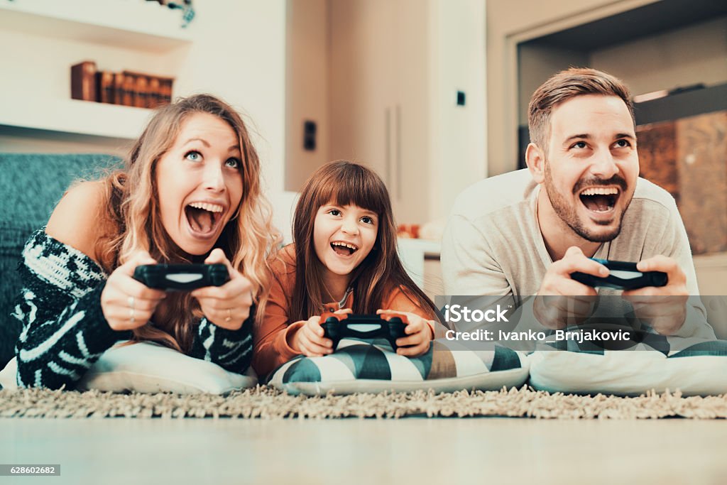 Competitive family playing video games at home Happy family- father, mother and daughter playing a video game at home. Family Stock Photo