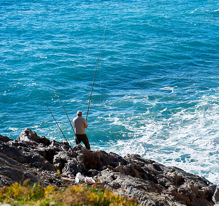 Genoa, Italy - December 18, 2012: Man with a fishing rod on the coast. Liguria. Italy