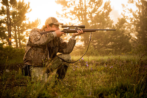 Hunter shooting with rifle Portrait of a hunter while crouching and aiming with rifle at his prey. hunting sport stock pictures, royalty-free photos & images