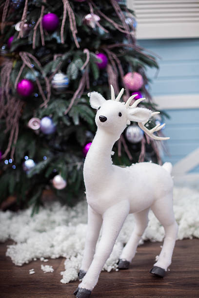 istock White deer toy near Christmas tree with unusual ornament. 628611744