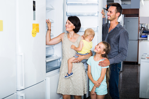 smiling family with two children choosing new fridge in warehouse