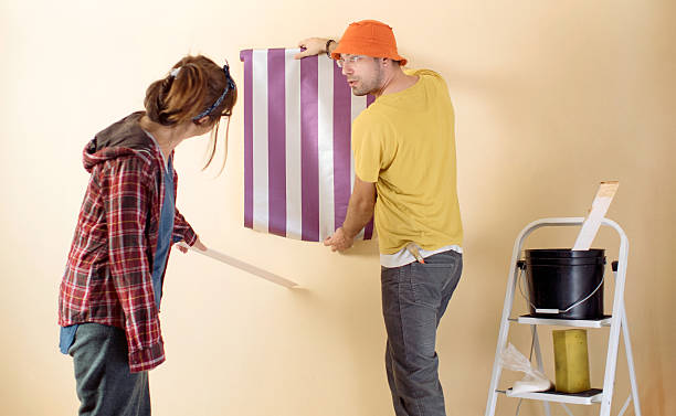 istock Friends applying wallpaper on wall in new home 628617992