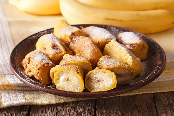 Traditional fried bananas sprinkled with powdered sugar close-up on the table. horizontal