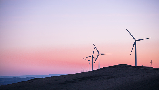 Horizontal axis wind turbines in the agricultural field under the clear sky at sunset, orange horizon over land at springtime, renewable energy sources