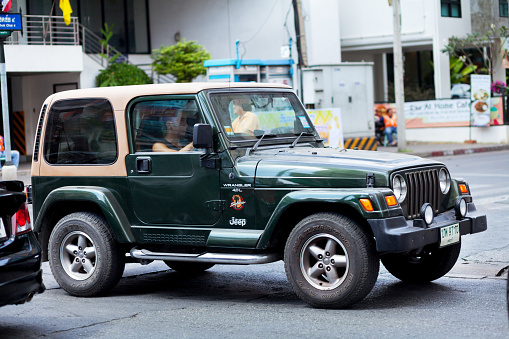 Bangkok, Thailand - February 21, 2015: Green colored Wrangler Jeep 4.0L is crossing junction on street Chokchai 4 in Ladprao. A thai man is drivng jeep.