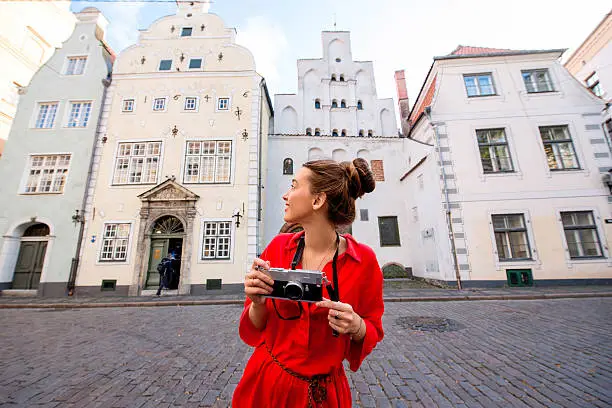 Portrait of a young female tourist with photo camera in front of the famous three brothers ancient houses in Riga. Woman having great vacations in Latvia