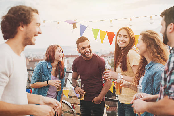 After work Multi-ethnic group of young people chatting and laughing on a rooftop party. teenage girls dusk city urban scene stock pictures, royalty-free photos & images