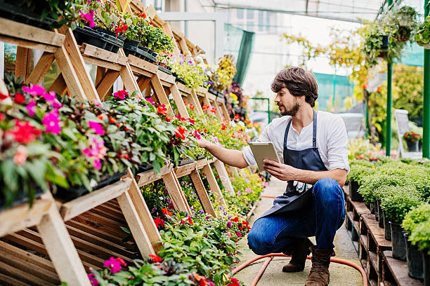 Gardener with digital tablet Young man holding a digital tablet working in a garden center. farm produce storage stock pictures, royalty-free photos & images