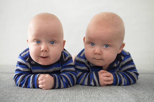 Identical twins Identical twins lying down on grey mattress blue brothers stock pictures, royalty-free photos & images