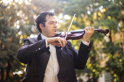 Violinist playing violin nature. About 35 years old, Caucasian male in formalwear.
