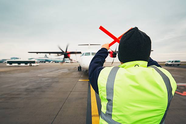 Busy day at the airport Prague, Czech Republic - December 1, 2016: Aircraft marshaller during visual signalling for pilots after landing. Vaclav Havel Airport Prague on December 1, 2016. taxiway stock pictures, royalty-free photos & images