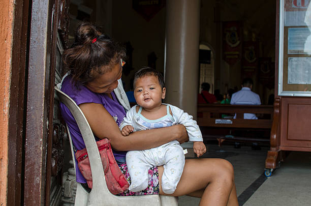 Mother cuddling baby at church portal door begging San Pablo City, Laguna, Philippines - December 3, 2016: Mother cuddling baby at church portal door begging for alms.  A common scene found in many Third World Countries. family mother poverty sadness stock pictures, royalty-free photos & images