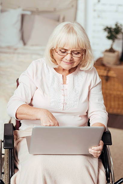 istock Pleasant elderly woman using laptop in the wheelchair 628759676