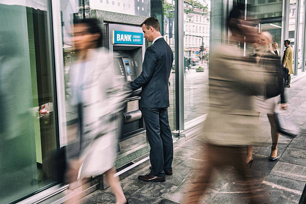 Man in front of an ATM machine Focus on man standing in front of an ATM machine on a city street, defocused incidental people. banks and atms stock pictures, royalty-free photos & images