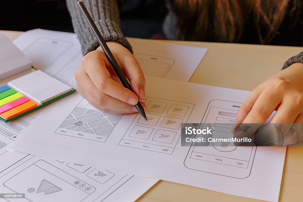 Designer wireframing a mobile App Designer wireframing a mobile App on wooden desk Graphic Designer Stock Photo