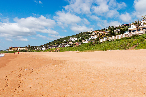Green lush dune vegetation, sand,  residential housing and blue cloudy skyline at Ballito beach near Durban, South Africa