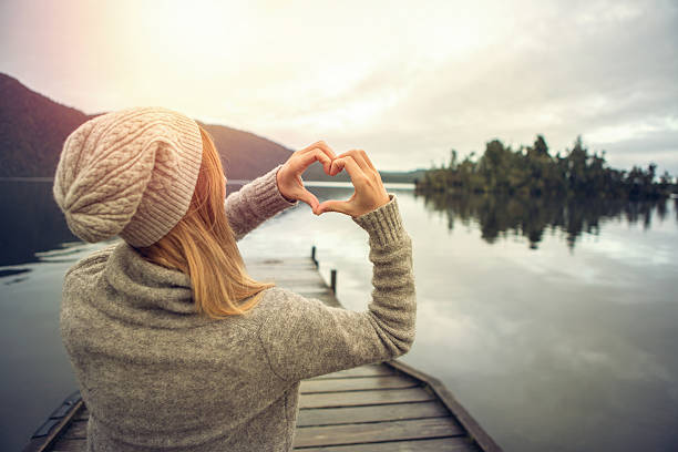 istock Young woman on lake pier, makes heart shape finger frame 628793042