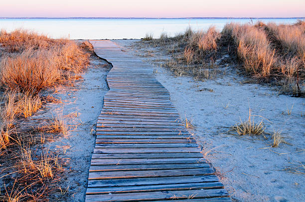 Wavy boardwalk across small dune Meandering boardwalk to beach reveals views of Buzzards Bay and Cape Cod cape cod stock pictures, royalty-free photos & images