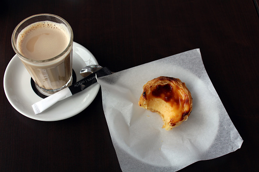 Coffee and sweet dessert on a white plate set on a black wooden table, Portugal