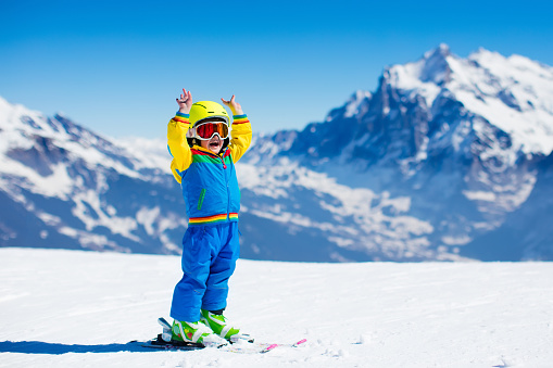 Three happy young skiers sits at mountain top and smiles. Winter vacations concept at ski resort
