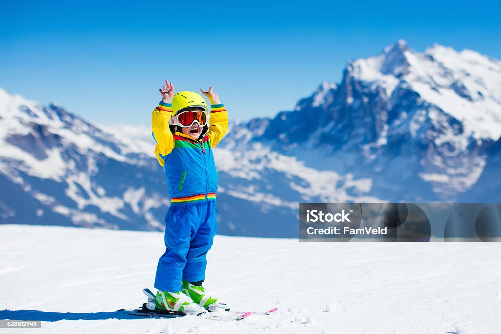 Ski and snow fun for child in winter mountains Child skiing in mountains. Active toddler kid with safety helmet, goggles and poles. Ski race for young children. Winter sport for family. Kids ski lesson in alpine school. Little skier racing in snow Skiing Stock Photo