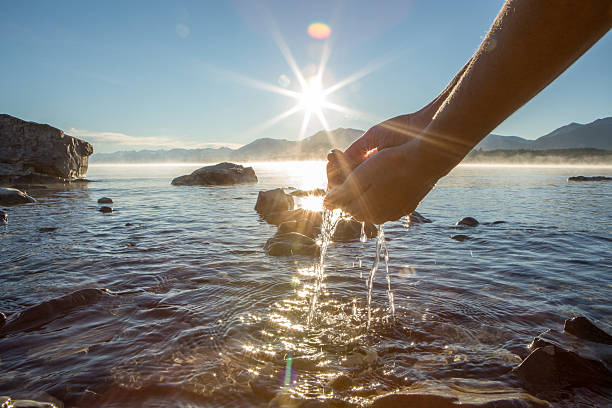 Human hand cupped to catch the fresh water from the lake, sunlight from sunrise passing through the transparence of the water.