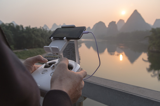 Yangshuo town, China - October 15, 2016 : Hands of a man operating drone DJI Phantom 4 during sunrise over Li River in Yangshuo Town, China on October 15, 2016.