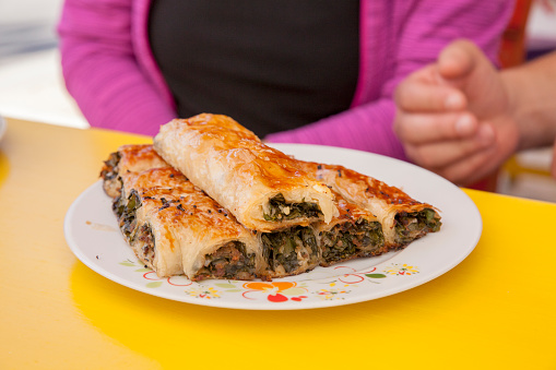 Spinach pastry, boreks in a white porcelain plate with olive oil, spinach leaves