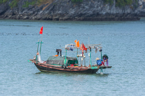 Halong Bay, Vietnam - November 15, 2015:  Vietnamese people working on their fishing boat on Halong Bay.  The woman wear the typical conical hat to protect her from the sun.  On the boat, fishing net, vietnamesa flag and clothesline.