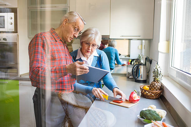 Cheerful senior couple preparing healthy meal using online recipe