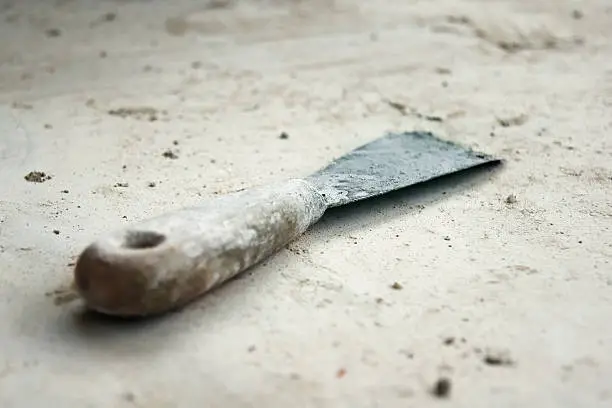 Close-up of an old and dirty putty-knife which lies on an dirty concrete floor.