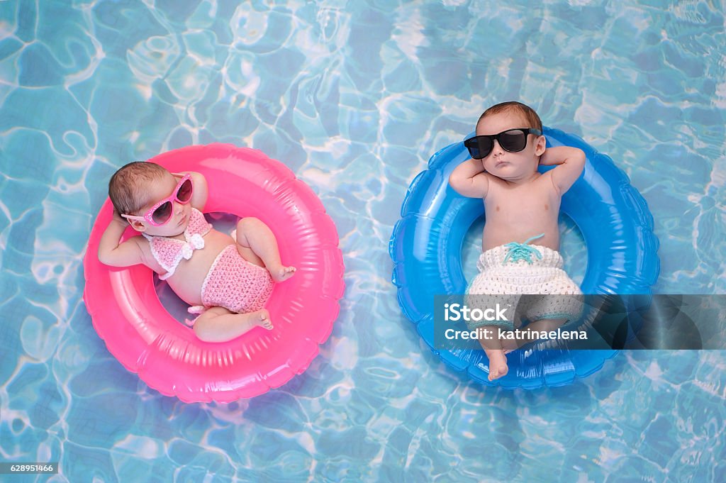 Baby Twin Boy and Girl Floating on Swim Rings Two month old twin baby sister and brother sleeping on tiny, inflatable, pink and blue swim rings. They are wearing crocheted swimsuits and sunglasses. Baby - Human Age Stock Photo