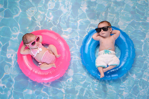 Baby Twin Boy and Girl Floating on Swim Rings Two month old twin baby sister and brother sleeping on tiny, inflatable, pink and blue swim rings. They are wearing crocheted swimsuits and sunglasses. twin stock pictures, royalty-free photos & images