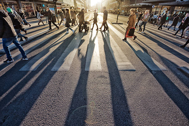 Pedestrians in silhouette, sunset in Stockholm Stockholm, Sweden - March 12, 2015: Pedestrians in silhouette on zebra crossing at Sergels Torg. Crowd casting long shadows. Low sun reflecting in asphalt and facades. Ahlens and subway entrance to the right. stockholm town square sergels torg sweden stock pictures, royalty-free photos & images