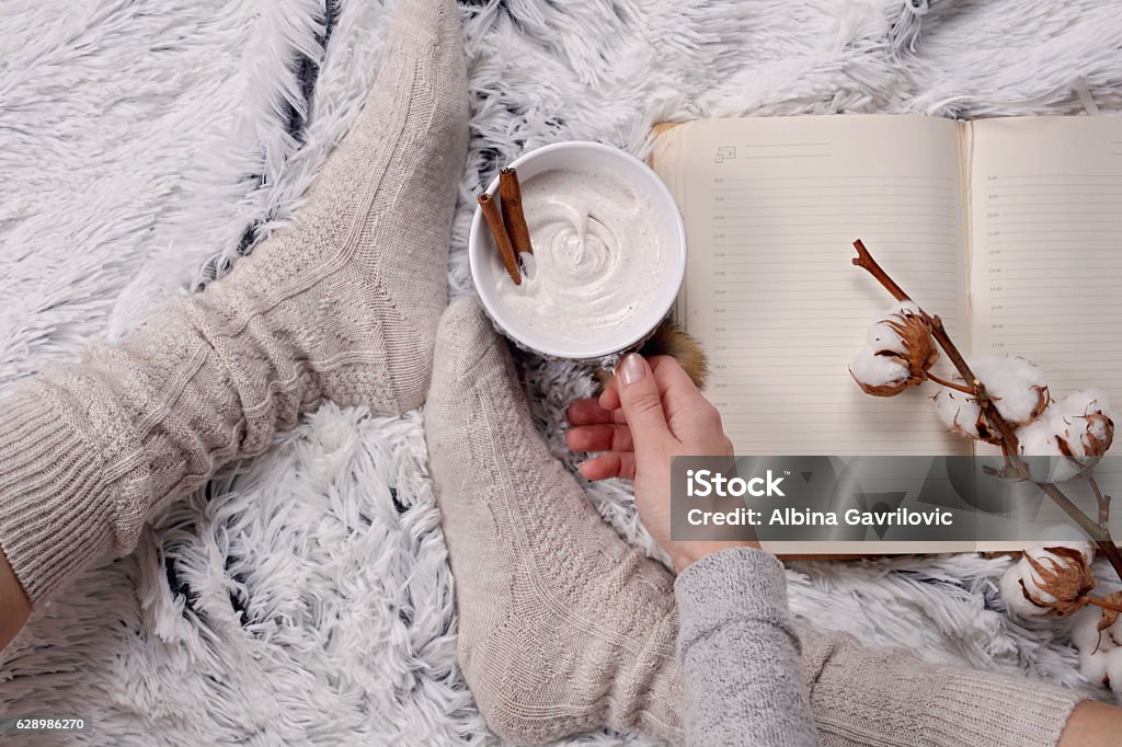 Woman wearing cozy warm wool socks, reading a book Woman wearing cozy warm wool socks, reading a book, drinking hot drink lose up. Warmth concept. Winter clothes Autumn Stock Photo